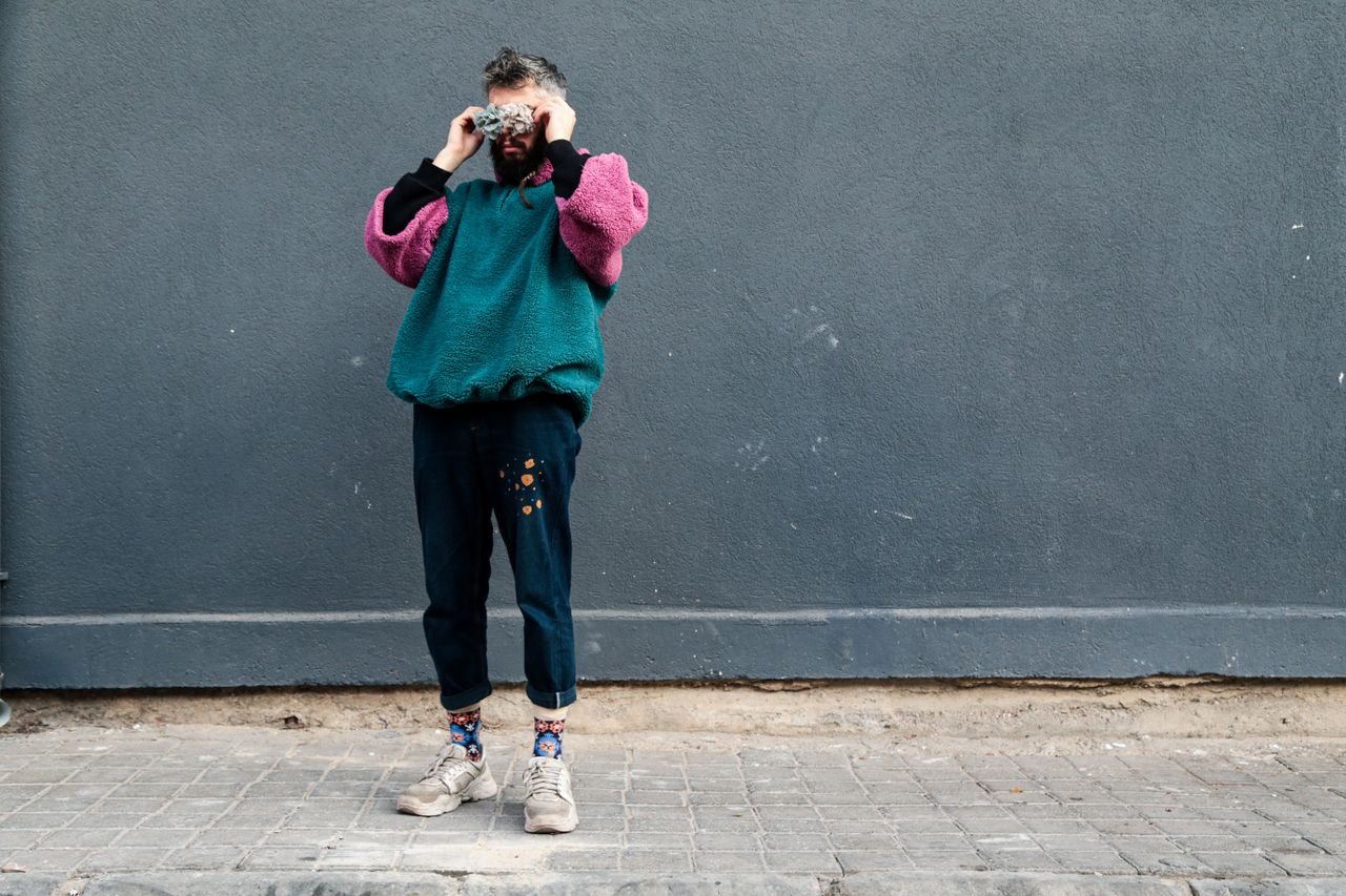 About Fashion model wearing colorful sweater and denim poses against gray urban wall.