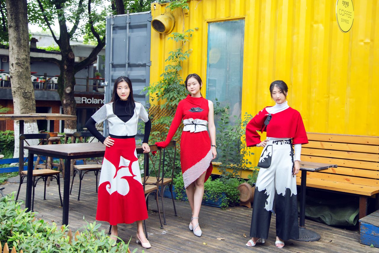 The Art of Drawing Readers In: Your attractive post title goes here Three women in stylish red and black outfits pose outdoors against a yellow container backdrop.
