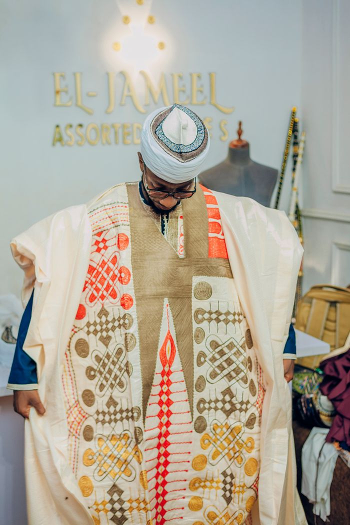Man wearing intricate traditional African attire inside a fashion studio setting.