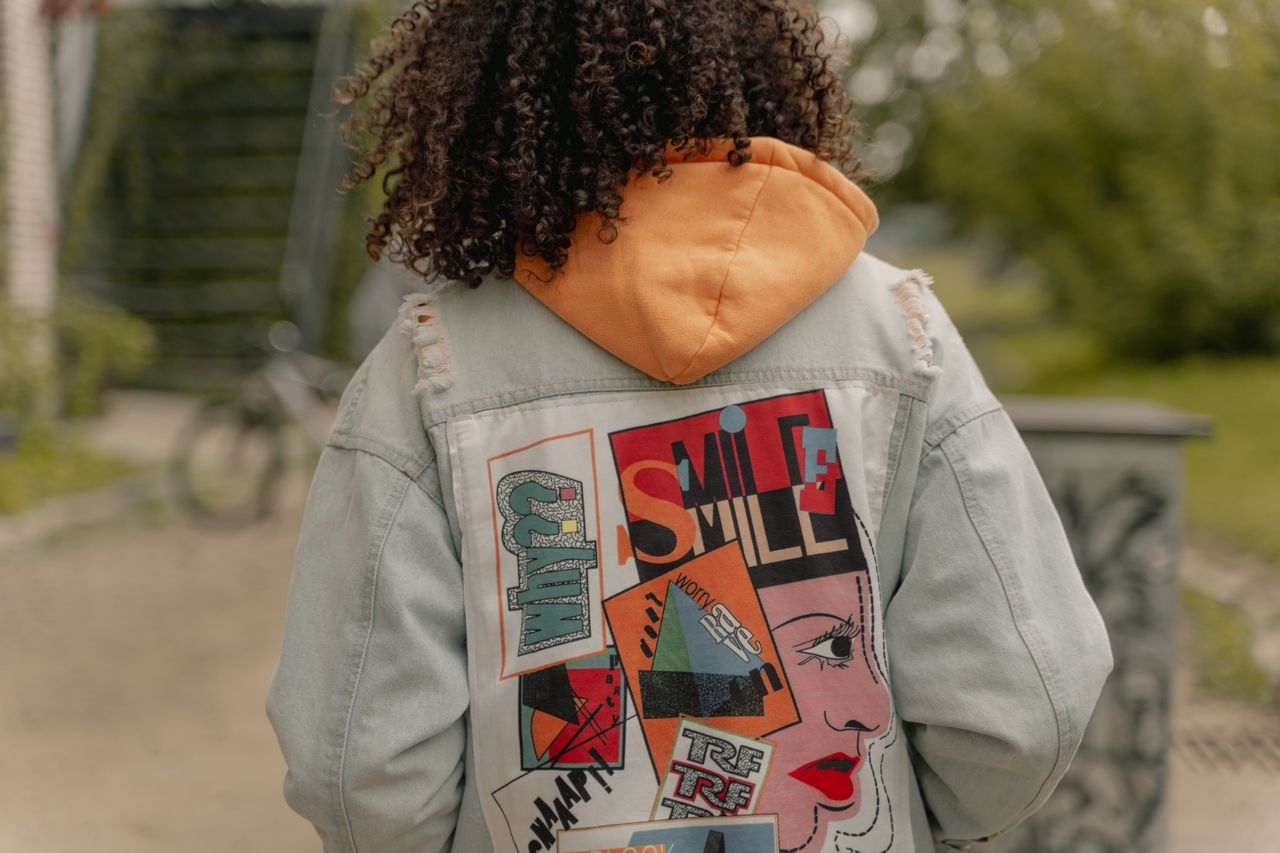 Back view of a stylish denim jacket with colorful design in a casual outdoor urban setting.